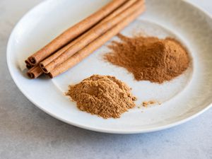 Mounds of cinnamon and cinnamon sticks on a white plate