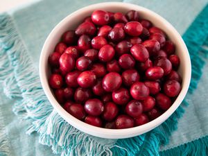 A white bowl of fresh cranberries set on a teal linen.