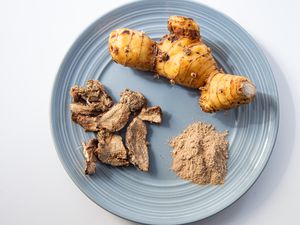 Fresh, dried, and powdered galangal spice on a blue plate