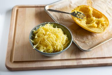 Roasted spaghetti squash in a bowl next to whole squash on sheet pan