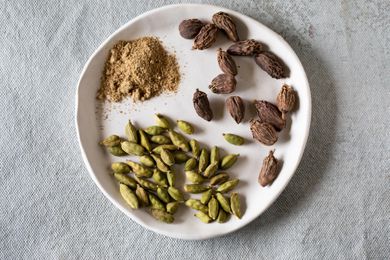 Ground cardamom and green and black cardamom pods on white plate