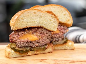Side view of a Jucy lucy burger cut in half to show the cheese in the middle and on a wooden cutting board.