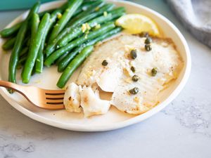 Lemon Butter Oven Baked Tilapia on a plate with a fork and green beans.