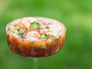 A parfait glass with mexican shrimp cocktail set on a table outside.
