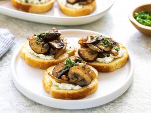 Three crostini topped with savory mushrooms and caramelized onions on a white plate.