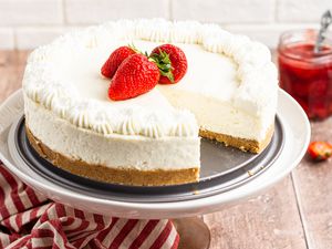 A cake stand with No bake cheesecake topped with fresh strawberries with a slice removed.
