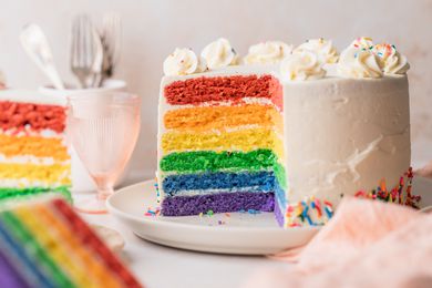 Rainbow Layer Cake on a Plate with a Portion Cut Out, Surrounded by More Cake