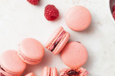 Overhead view of French macarons with raspberry buttercream filling and whole raspberries next to them.