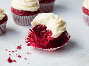 A red velvet cupcake set in a cupcake liner with a bite taken out of it.