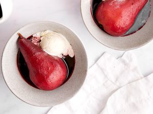 Two poached pears in small white bowls with ice cream.