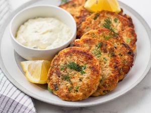 Salmon patties set on a plate with a dip and lemon.