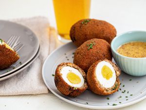 Scotch eggs in half on a plate with honey mustard dip.