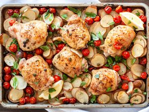Overhead view of sheet pan chicken thighs with tomatoes, potatoes, capers, and basil on a sheet pan.