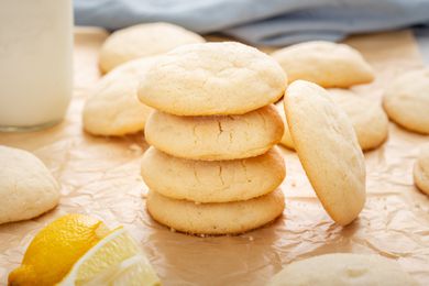A stack of soft lemon drop cookies on parchment with more cookies set around it.