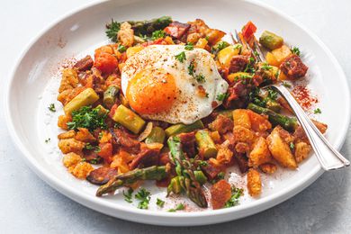 A white plate with Spanish Style Migas with Asparagus, Chorizo, Bacon, and Eggs.