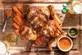 Smoked Spatchcock Chicken with Harissa Butter and Grilled Carrots on Cutting Board, Surrounded by Bowl of Harissa, Bowl of Herb, Kitchen Towel, and a Drink