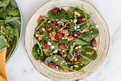 Spinach salad with grapes and bacon dressing on a ceramic plate.