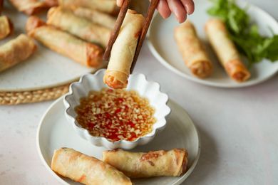 Dipping a spring roll into a sauce with more spring rolls on the plate and on a platter behind it.