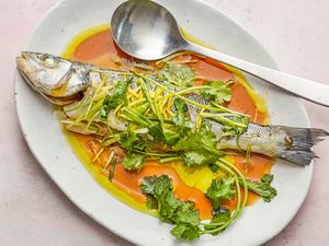 Overhead view of a steamed whole fish on a flatter and topped with sauce and herbs.