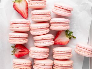 Overhead view of strawberry macarons lined up on their side with halved strawberries set in-between the rows.