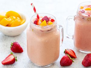 Strawberry peach smoothie with a straw and chopped fruit on top and around the glass cup.