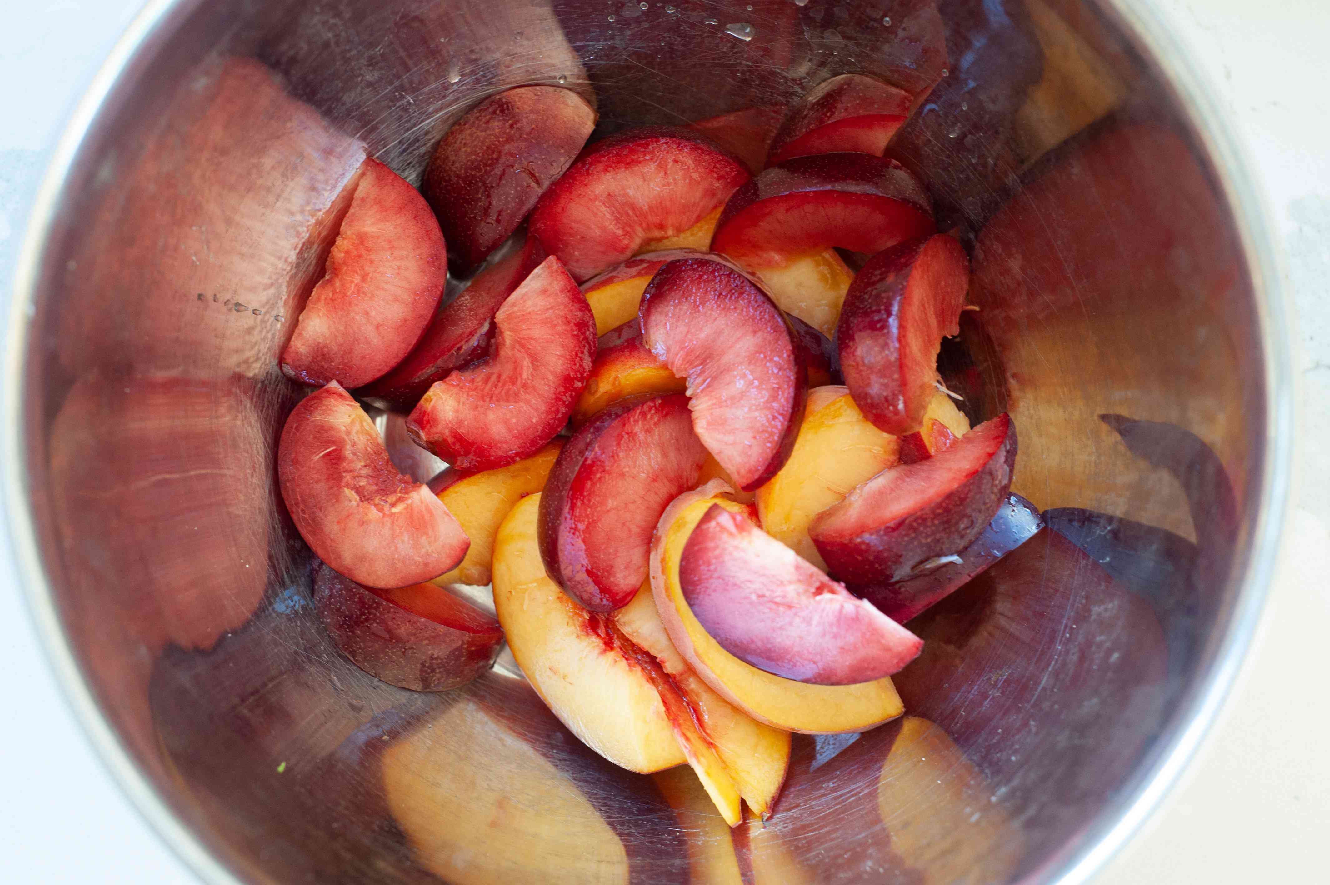 Plums and peaches cut into wedges and set in a bowl to make a summer-y salad with stone fruit and frisée.