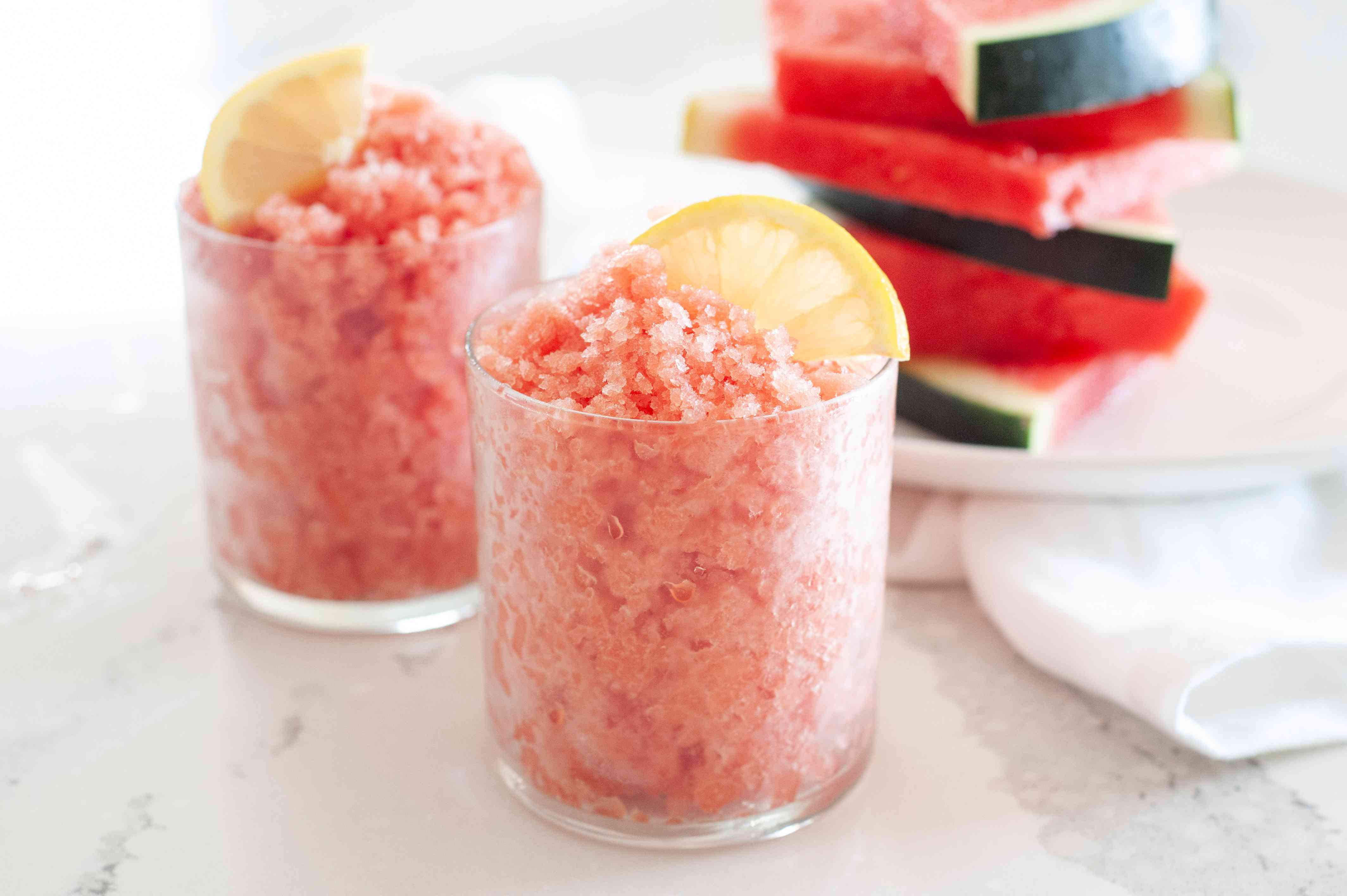 Side view of two glasses with watermelon granita and garnished with lemon slice.