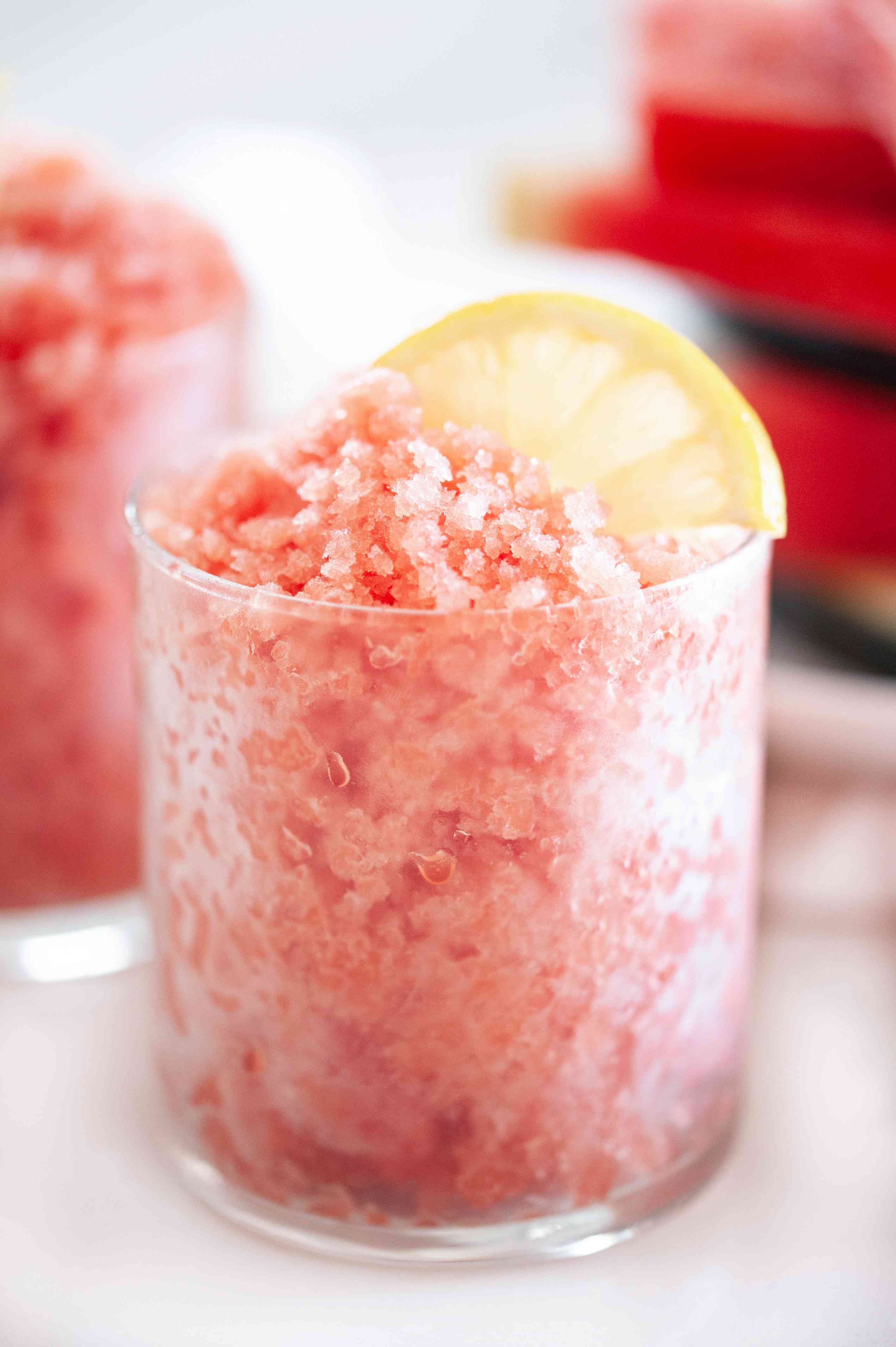 Side view of a watermelon granita with a stack of watermelon behind it.