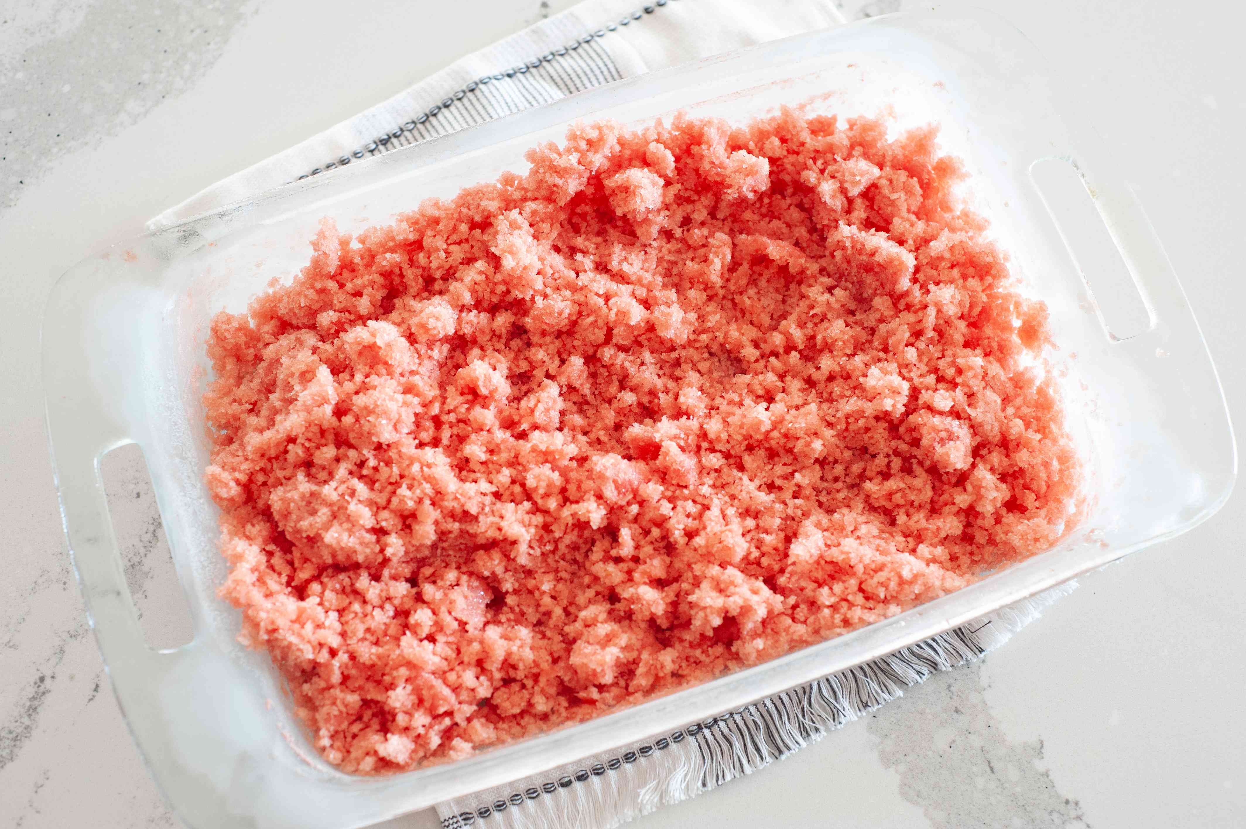 How to make a watermelon granita recipe showing frozen watermelon mixture that's been scraped in a glass baking pan.