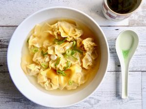 Overhead view of a bowl of pork and ginger wontons in chicken soup.