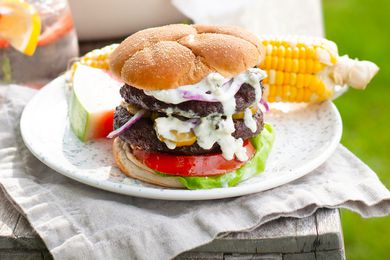 Burger dripping with blue cheese sauce, on plate with corn and watermelon