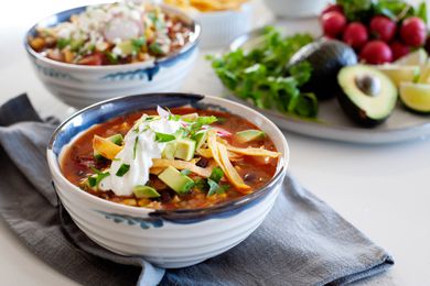 Meatless tortilla soup in a bowl topped with shredded cheese, sour cream, and tortilla strips.